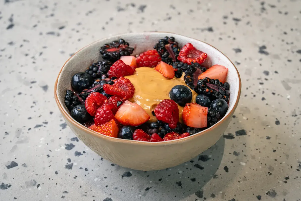 Blackberries, blueberries, raspberries and strawberry chunks ringing a glossy pool of tan nut butter in a small cream bowl
