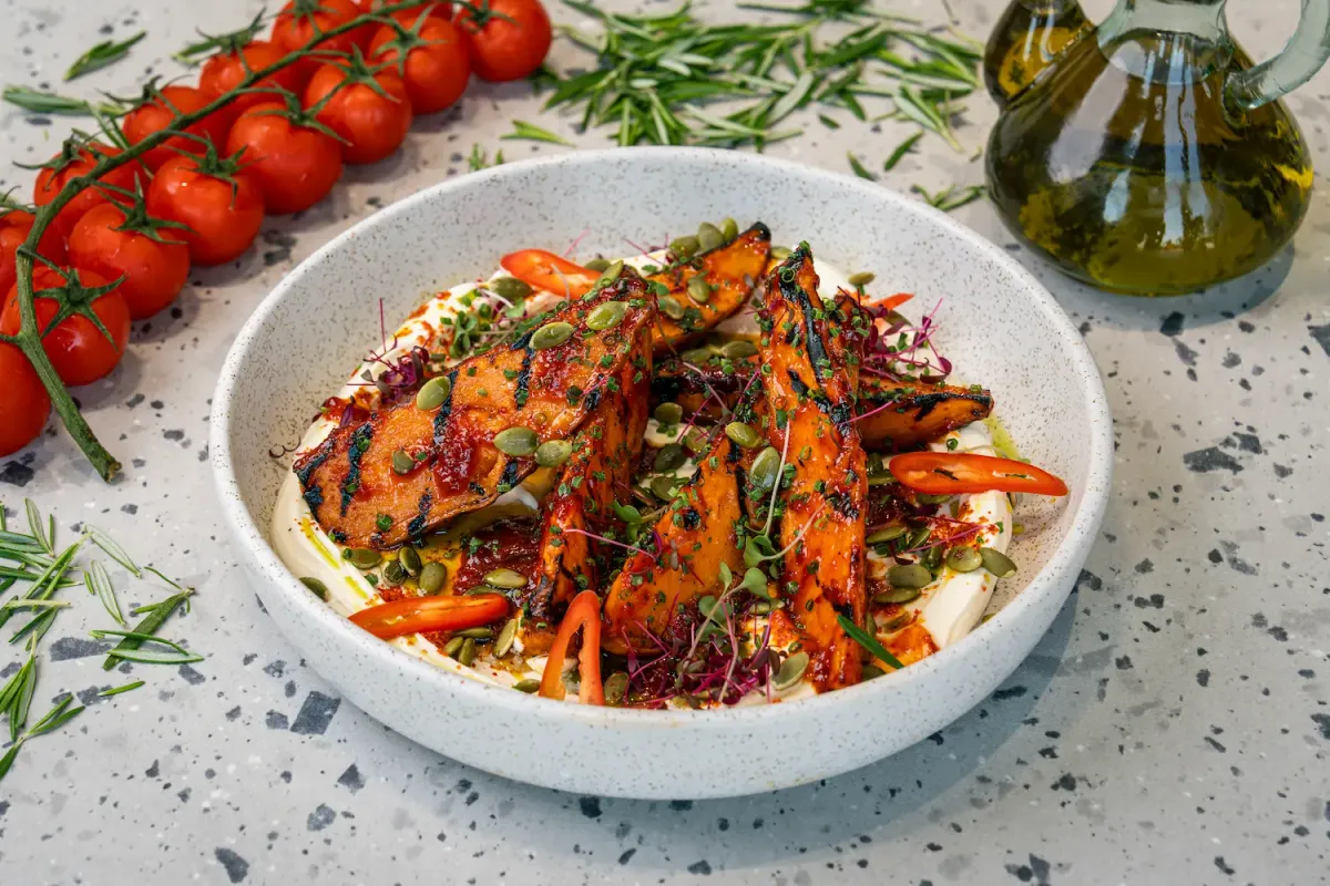 Griddle-striped sweet potato wedges in a glossy red glaze, set on a pool of white cream with pumpkin seeds, chilli slices and micro herbs