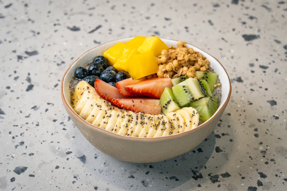 Chia-seed pudding under mango wedges, blueberries, granola, kiwi and strawberry, ringed by chia-dusted banana slices in a stone bowl