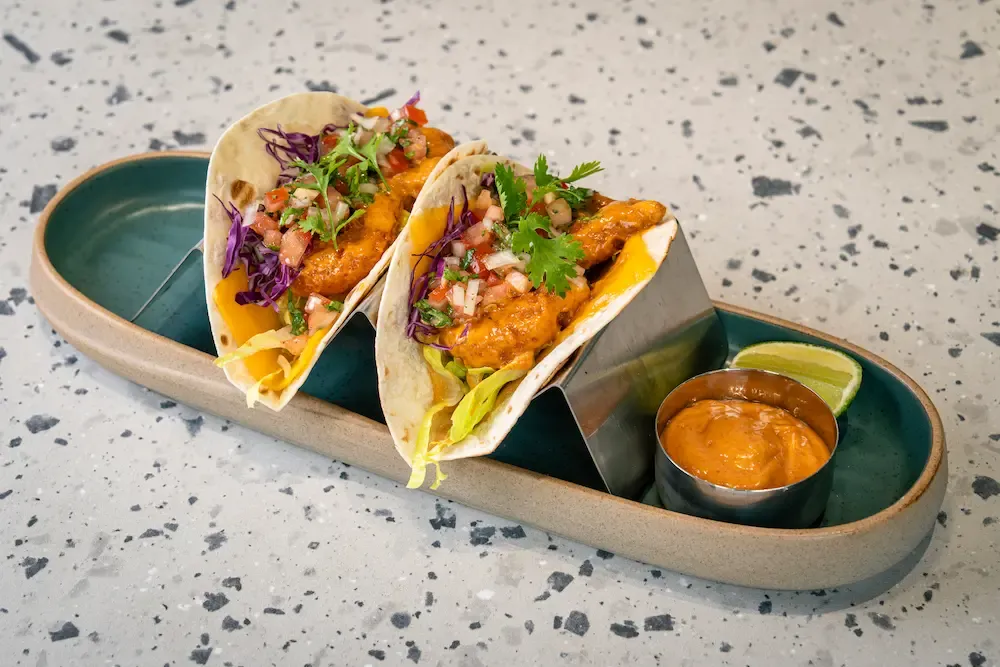 Glossy orange prawns with tomato salsa, purple cabbage and coriander in soft tortillas, shredded cheddar spilling out, lime wedge alongside