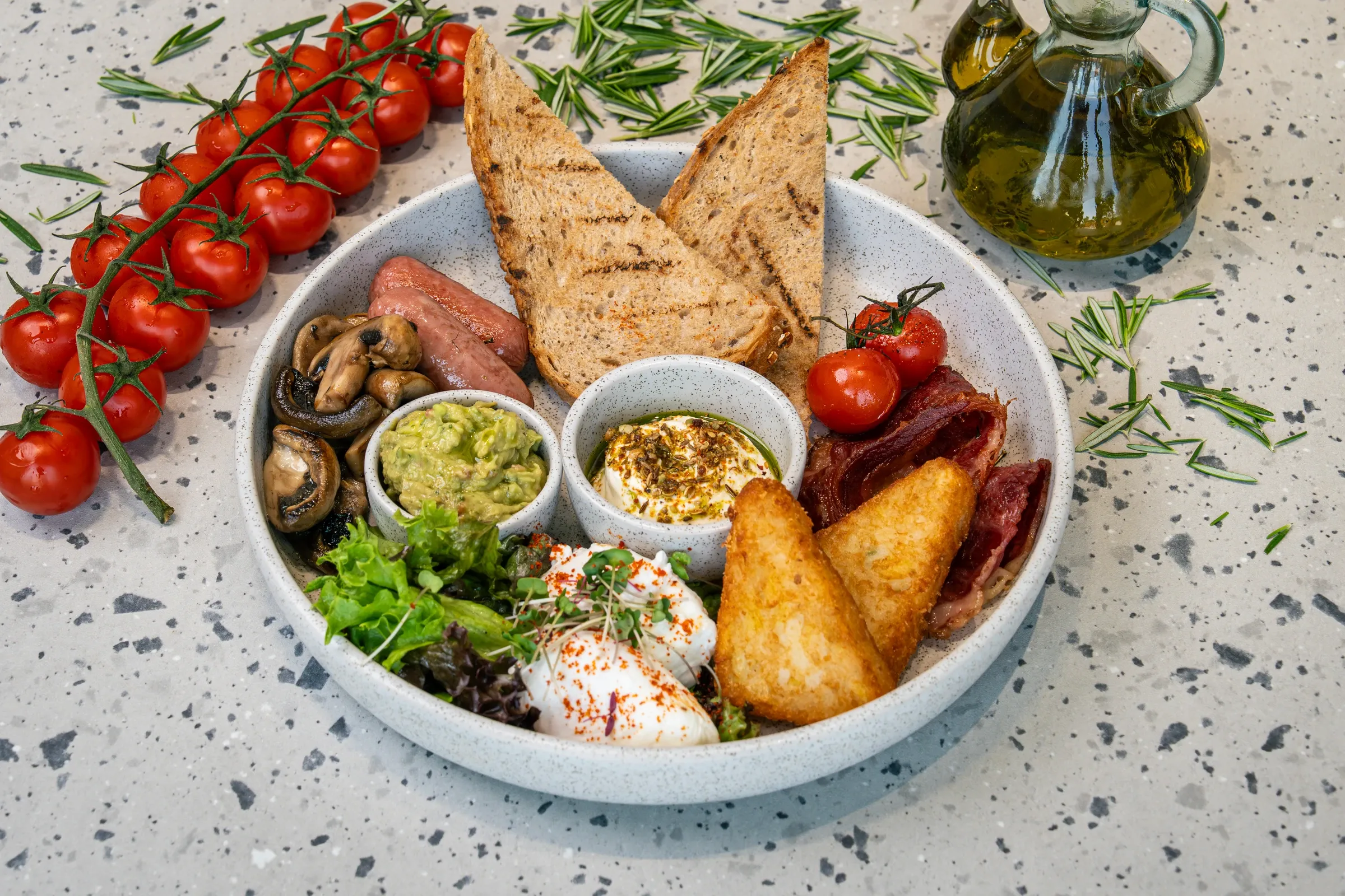 Shallow bowl ringed with mushrooms, sausage, griddled toast, vine tomatoes, beef bacon, hash browns and poached eggs, plus pots of guacamole and labneh