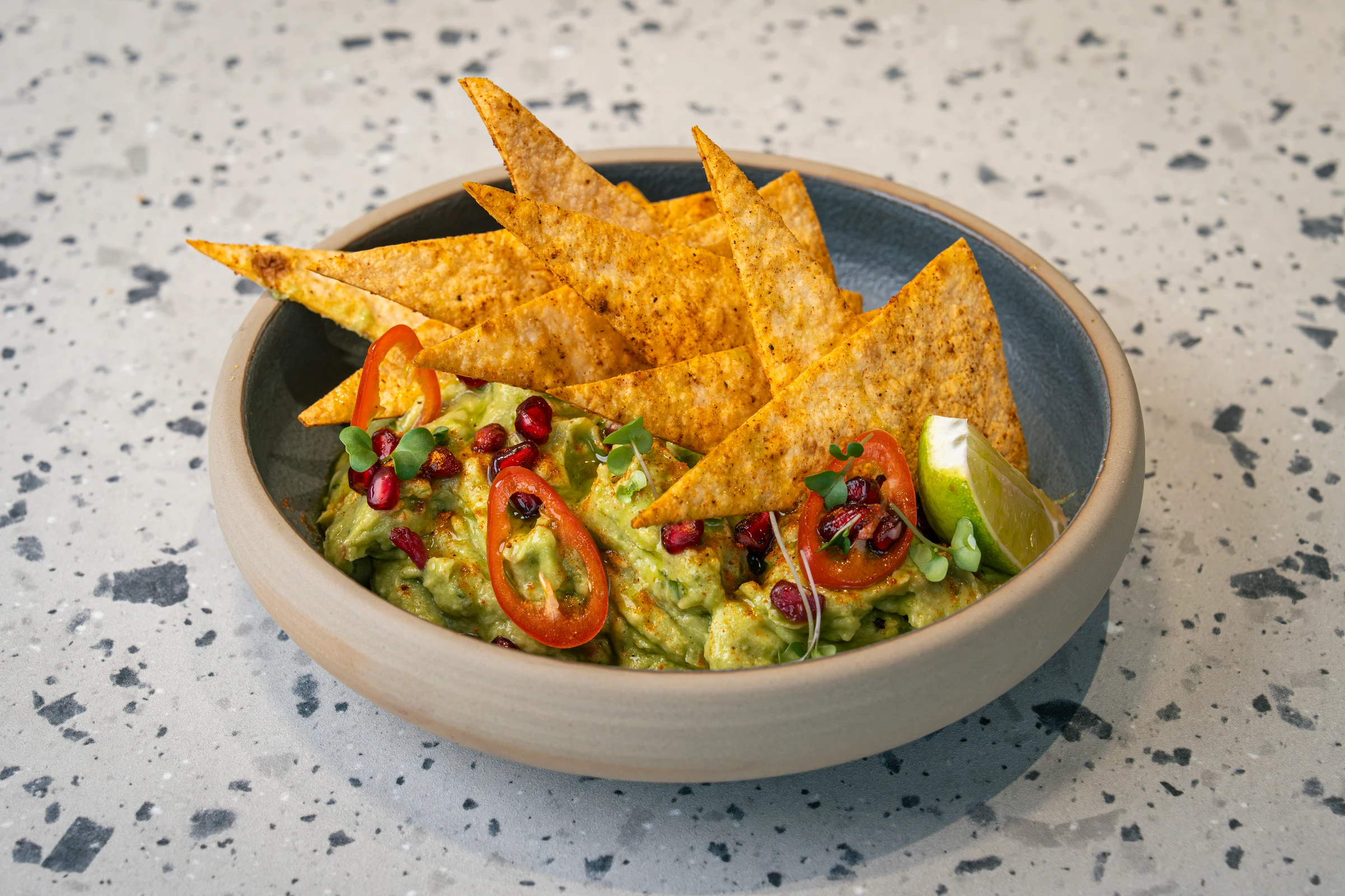 Chunky guacamole studded with pomegranate seeds, red chilli rings and a lime wedge, spiked with paprika-dusted tortilla shards