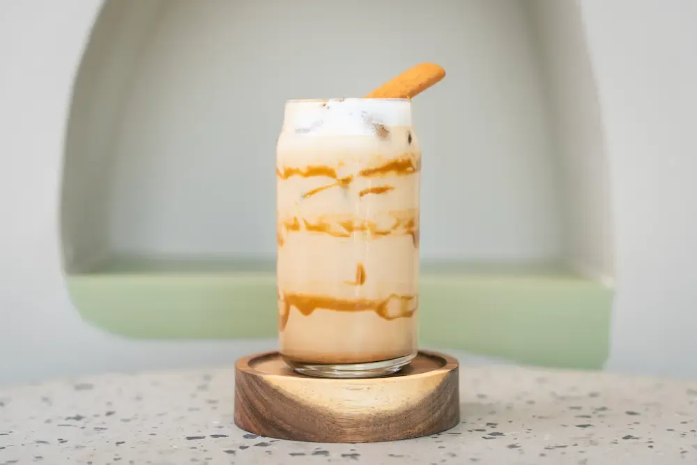 Caramel iced latte in a can-shaped glass with thick Biscoff syrup streaked down the inside, foam and a biscuit resting on top