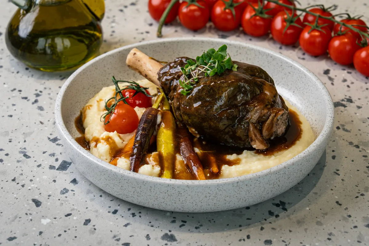 Bone-in lamb shank glazed in dark gravy over mashed potato, with baby heirloom carrots, a vine tomato and micro leaves on top