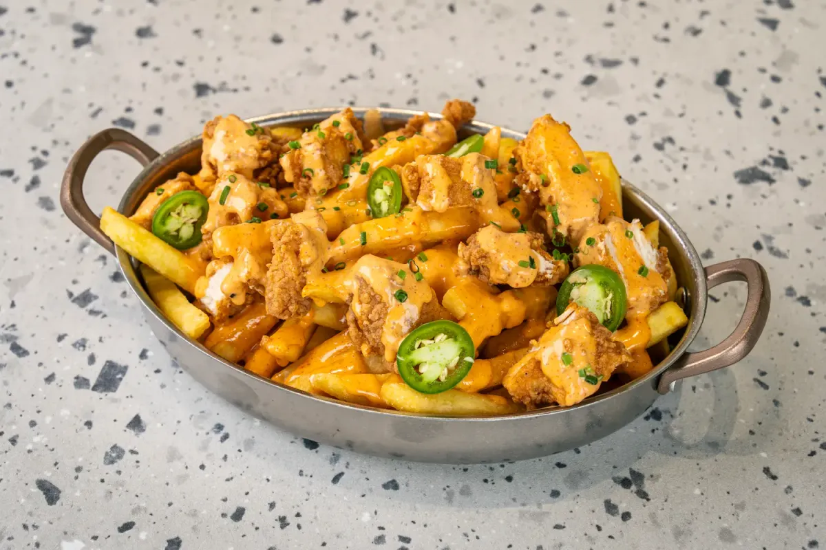 Chips smothered in orange sauce with breaded chicken pieces, green jalapeño rings and chopped chives, heaped in a steel pan