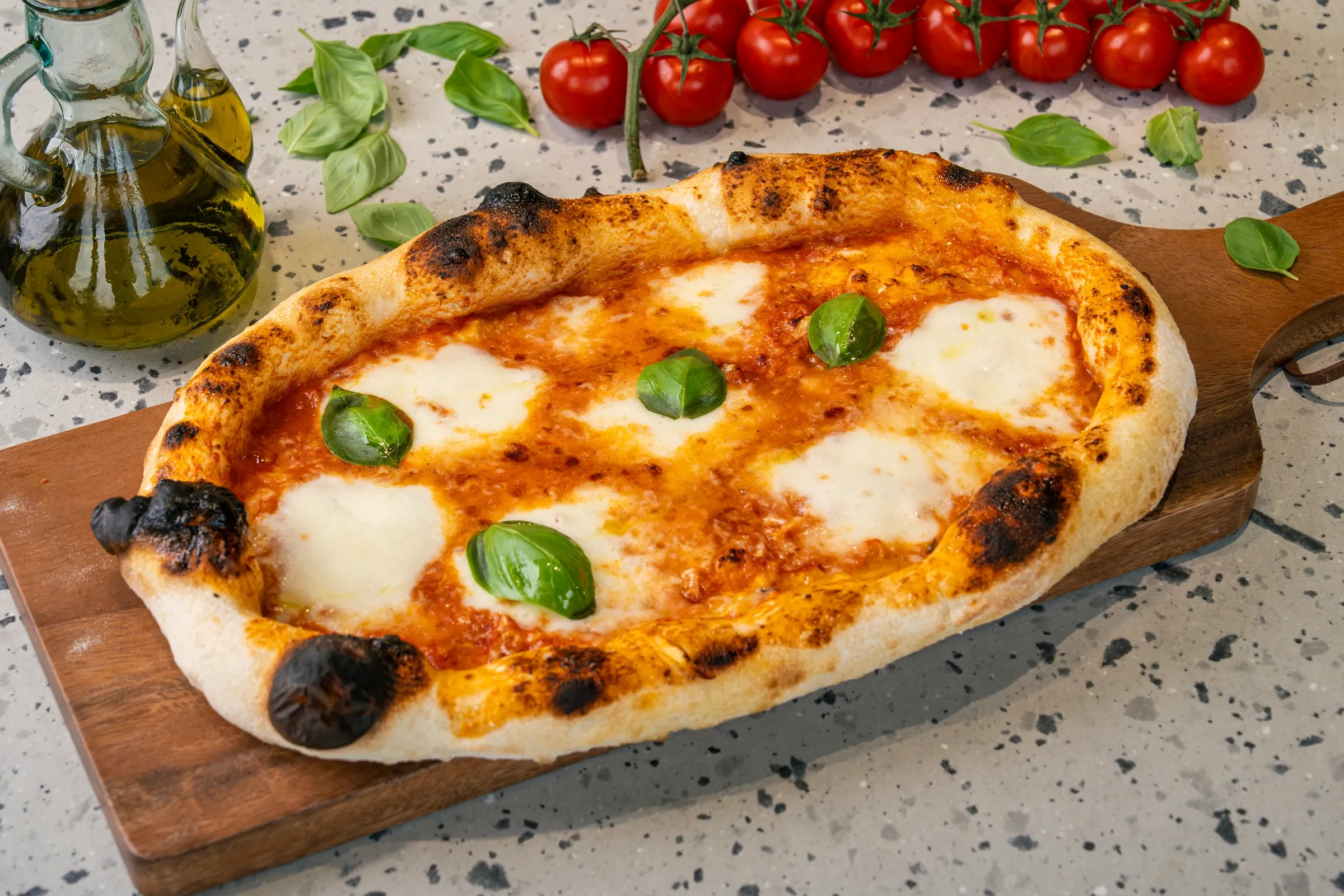 Oval flatbread of tomato sauce and pools of molten mozzarella with whole basil leaves, blackened bubbles on the raised crust