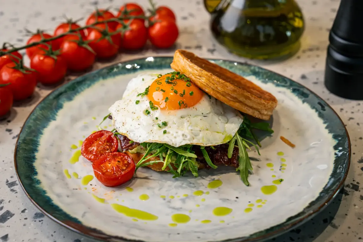 Guacamole, rocket and beef bacon on a croissant base under a fried egg with a deep orange yolk, olive oil dotted around the plate