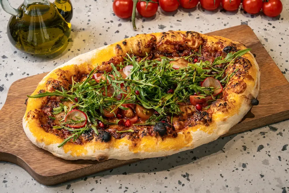 Brick-red pepper paste and melted cheese under a mound of rocket, radish slices, cherry tomatoes and pomegranate seeds
