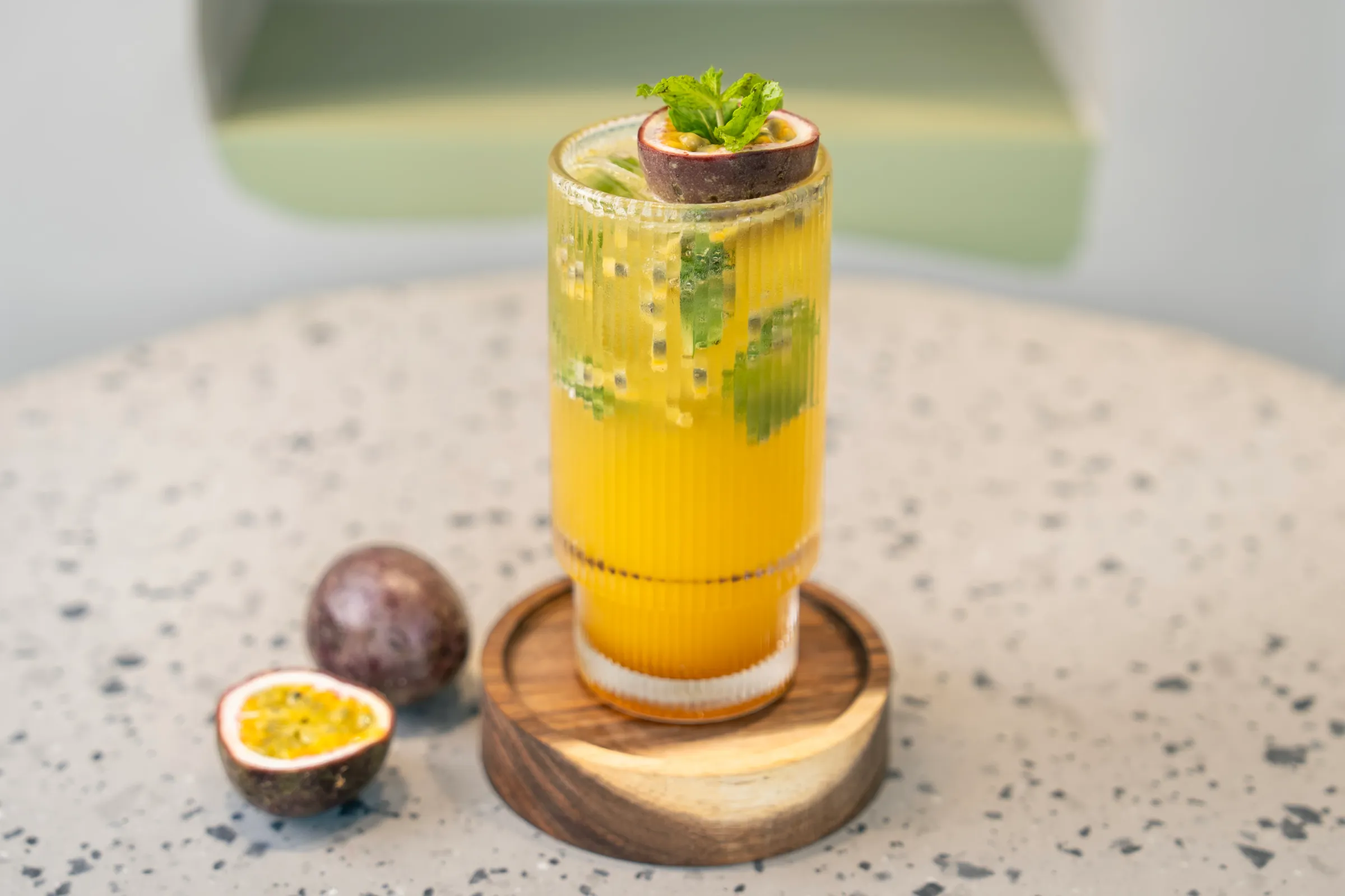 Golden drink flecked with passion fruit seeds and mint, a halved fruit and mint balanced on the rim, whole and cut fruit alongside