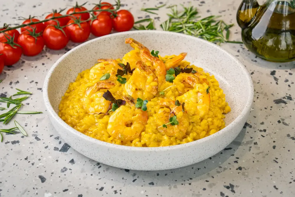 Deep yellow saffron risotto in a white bowl with pink-tailed prawns fanned across the top and small green and purple micro leaves