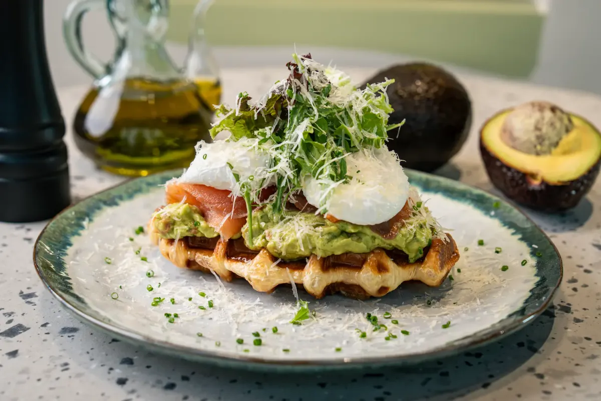 Waffle-pressed croissant under smashed avocado, smoked salmon and two poached eggs, buried in finely grated parmesan and leaves