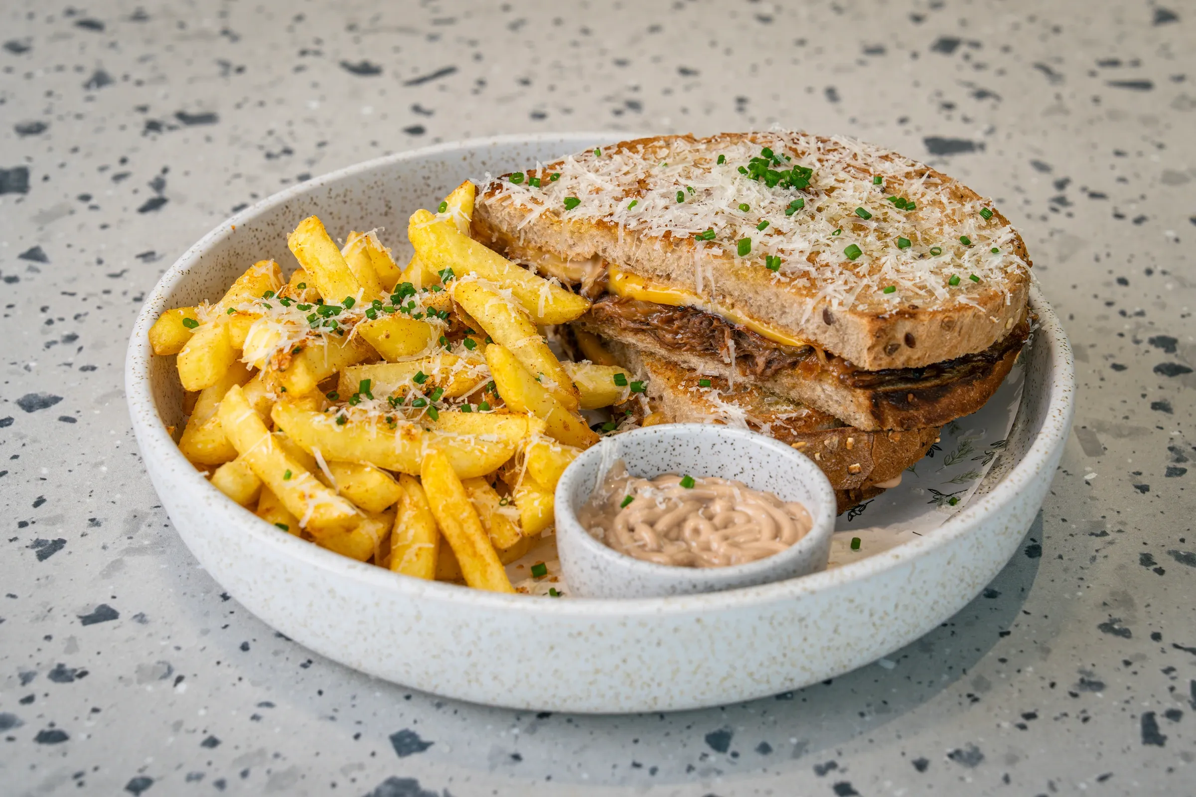 Toasted seeded bread stacked around shredded braised beef, dusted with grated cheese and chives, chips and a dip pot in the same bowl