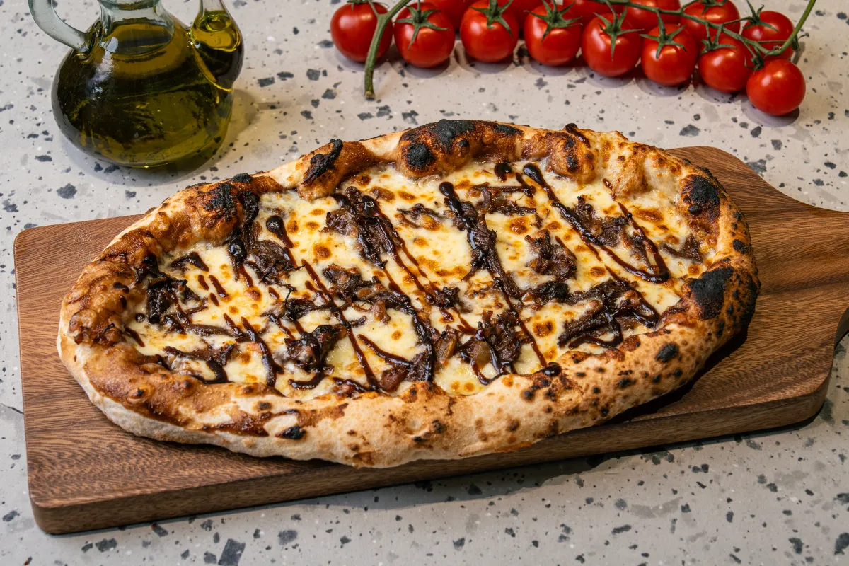 Oval flatbread under melted mozzarella with dark shredded beef and caramelised onion, criss-crossed with balsamic glaze