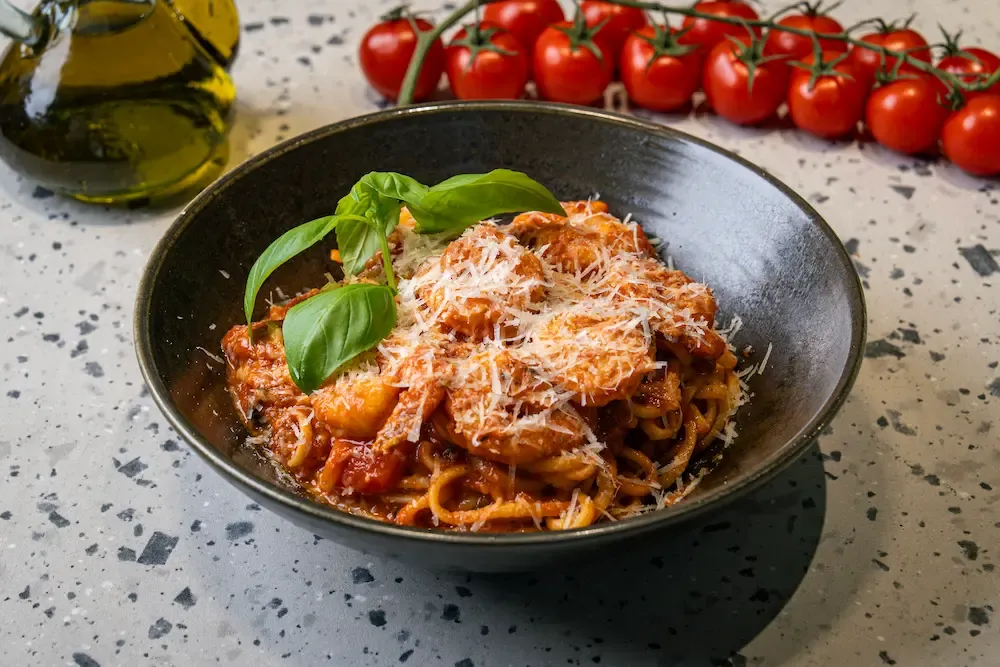Linguini and prawns in tomato sauce in a black bowl, buried under finely grated parmesan with a sprig of basil at the side