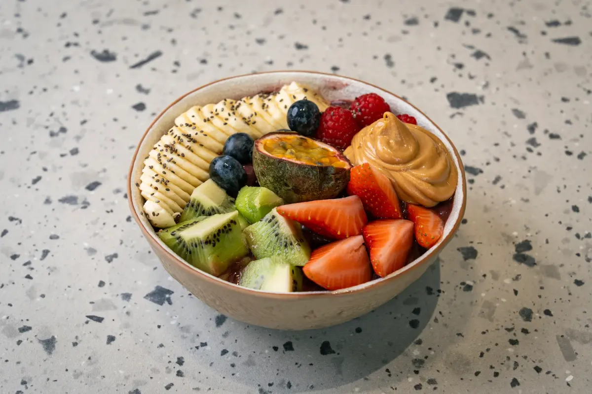Purple açaí under sliced banana with chia, kiwi, strawberries, raspberries, blueberries, half a passion fruit and a peanut butter swirl