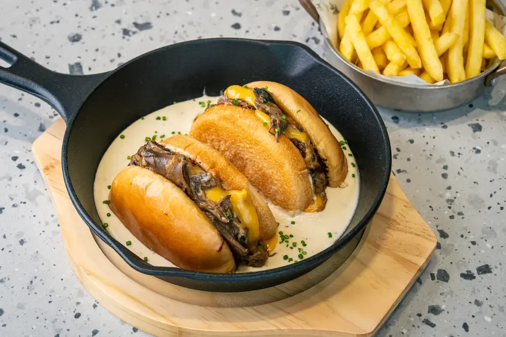 Three brioche sliders sitting in pale sauce in a cast-iron pan, cheddar and dark mushrooms spilling out, chives scattered over
