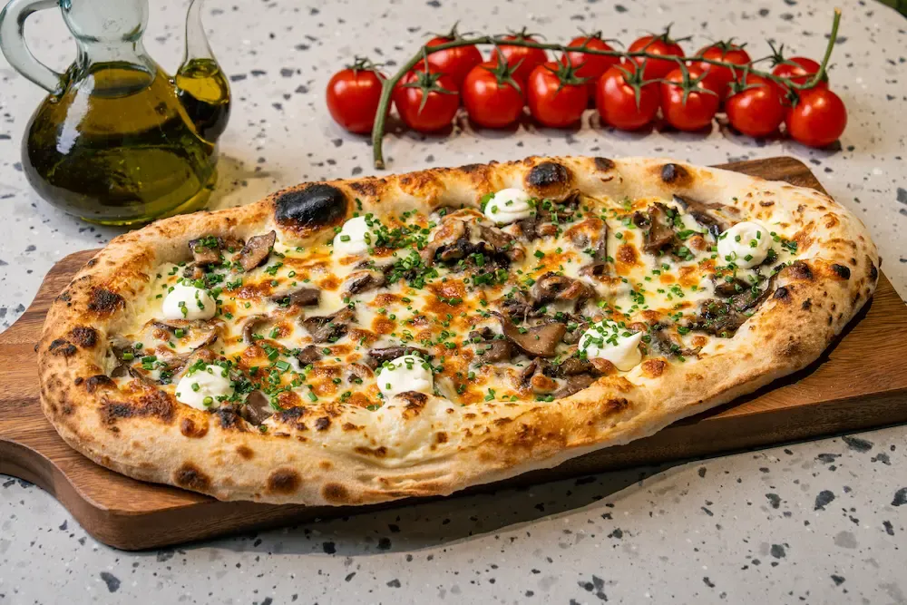 Sliced brown mushrooms and browned mozzarella on a puffed oval flatbread, dotted with white sour cream and chopped chives