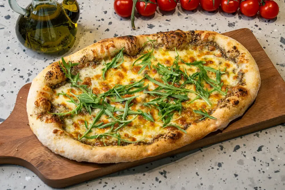 Golden bubbling cheese edged with dark za'atar on a round flatbread, topped with a loose pile of rocket leaves