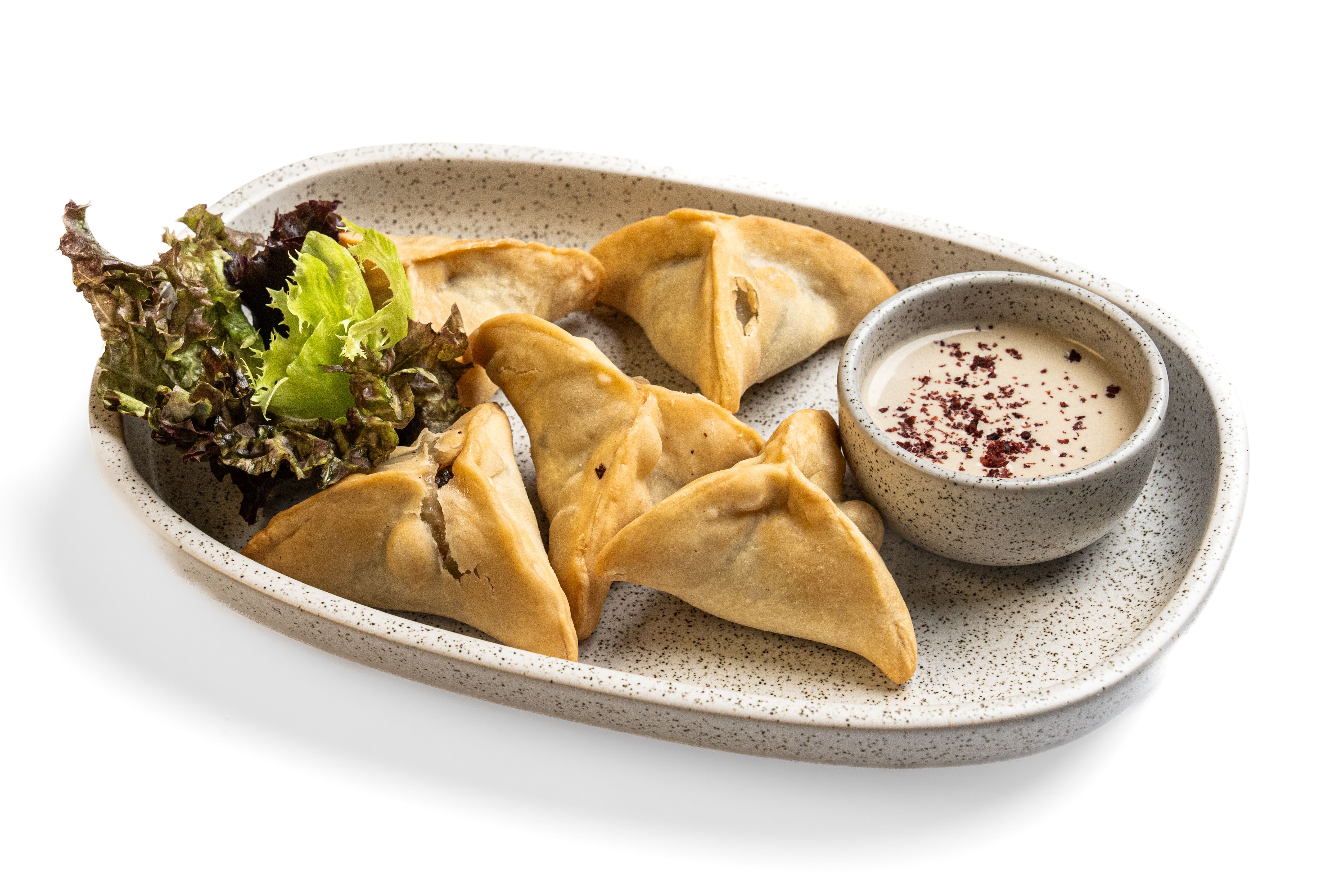 Golden folded pastries served with a dipping sauce and fresh leaves