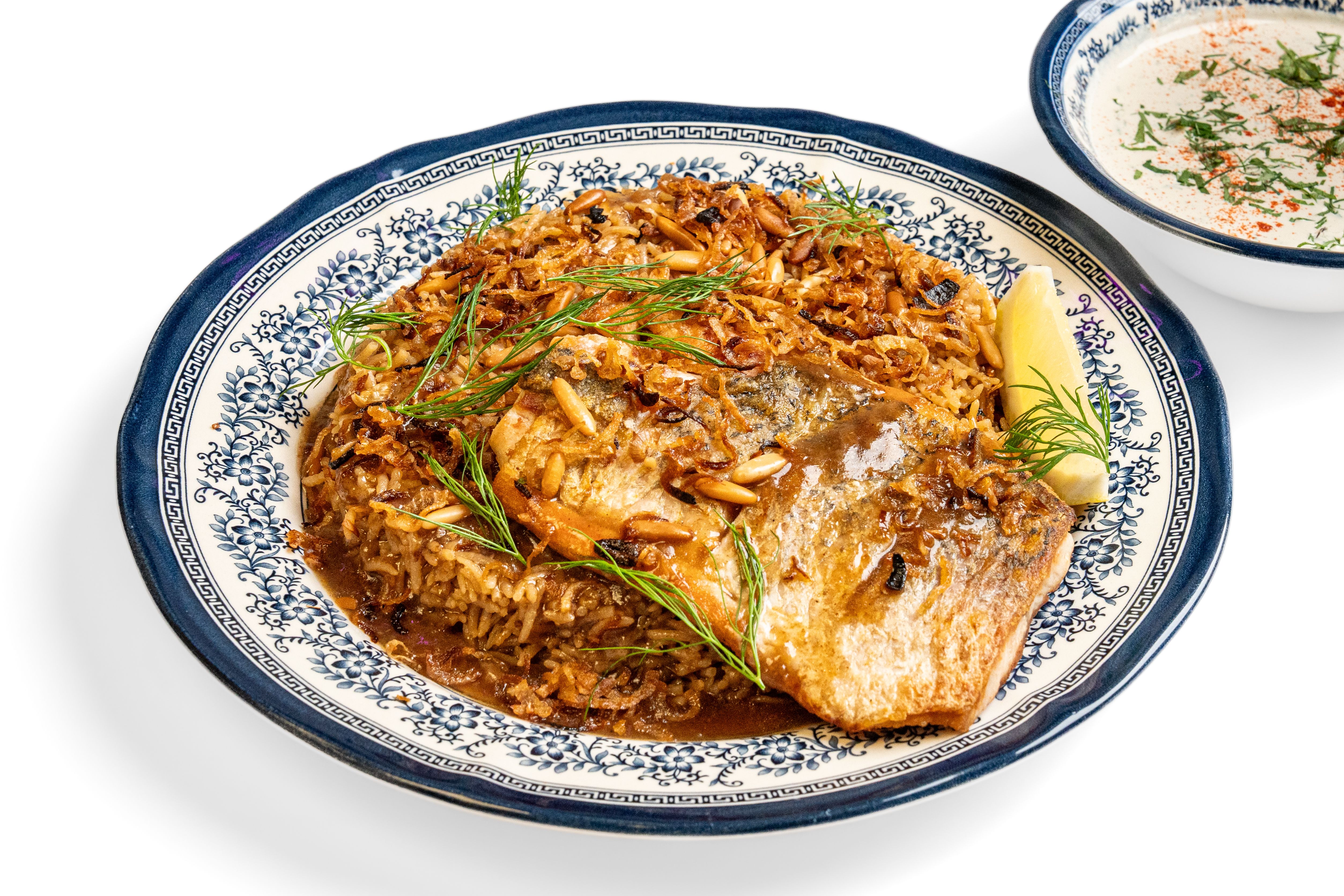 A fish fillet over rice with crisp onions and a lemon wedge