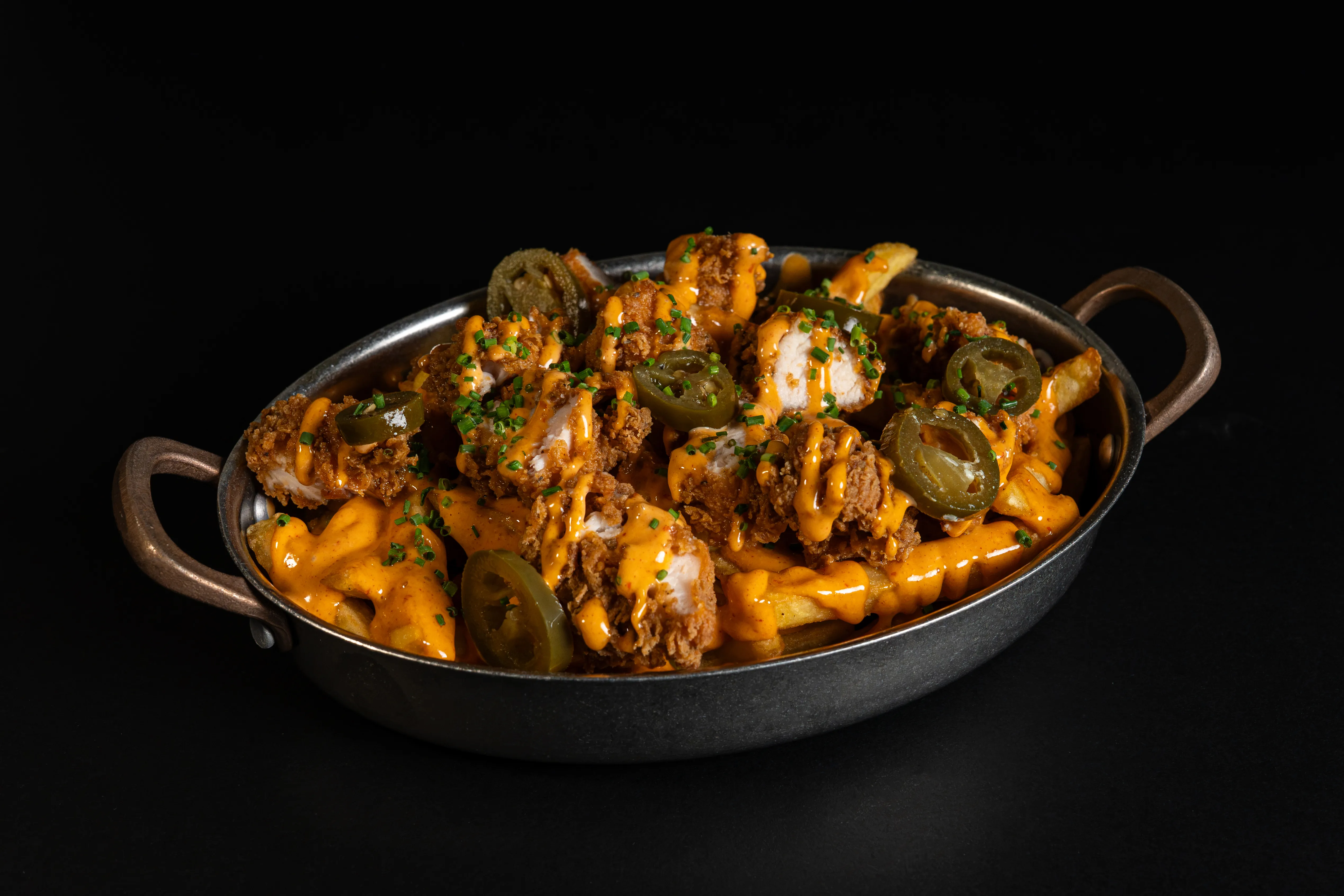 Loaded fries with toppings in a small handled pan