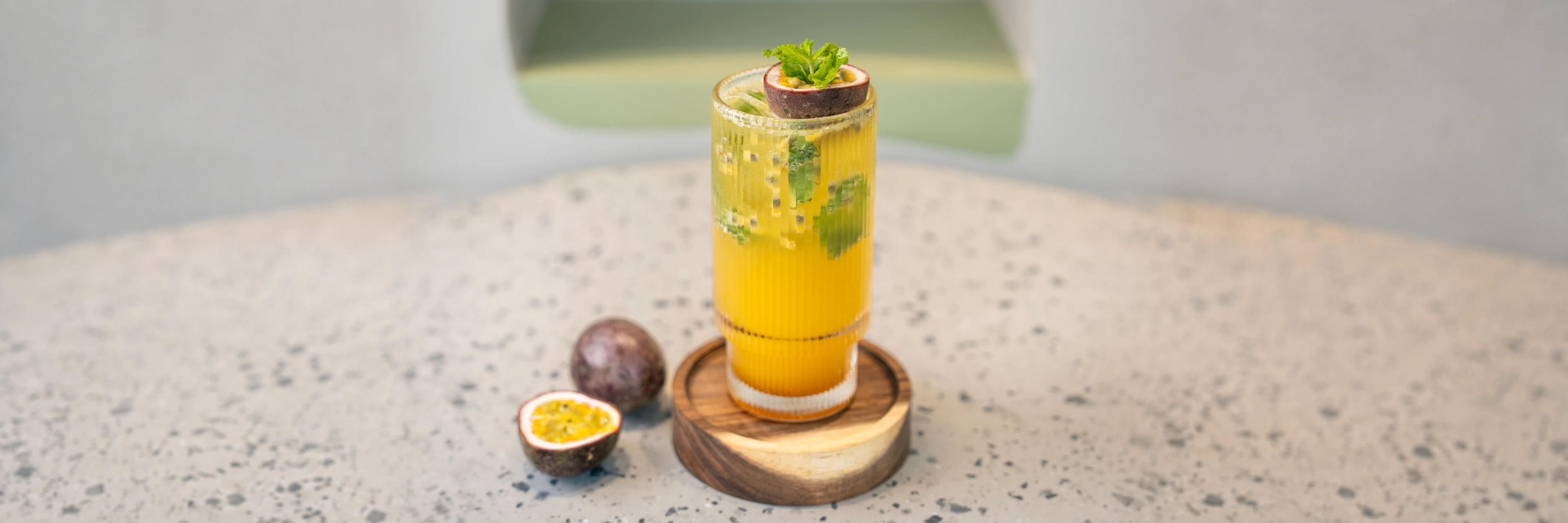 Golden drink flecked with passion fruit seeds and mint, a halved fruit and mint balanced on the rim, whole and cut fruit alongside