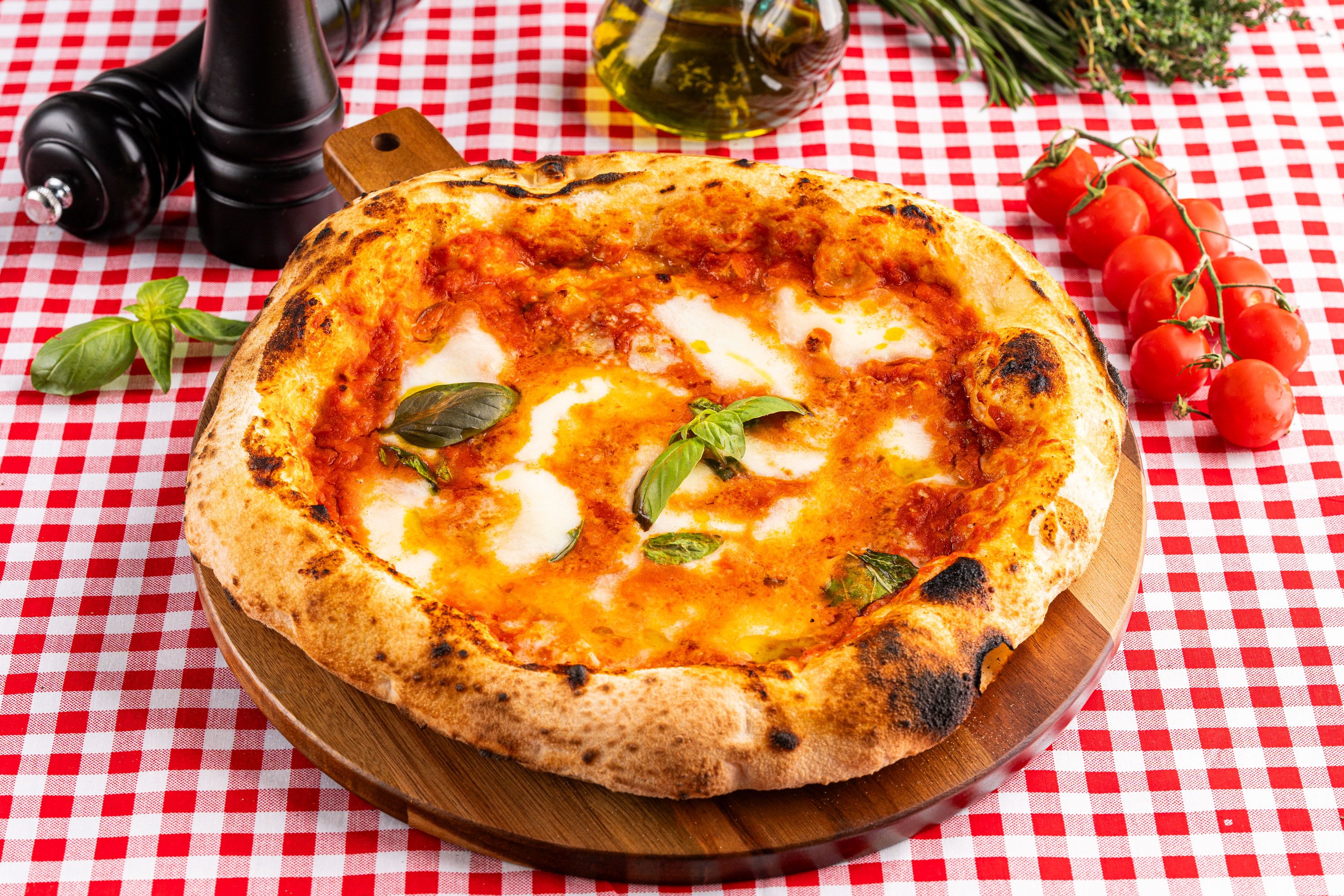 A blistered tomato and basil pizza on a wooden board and red checked cloth