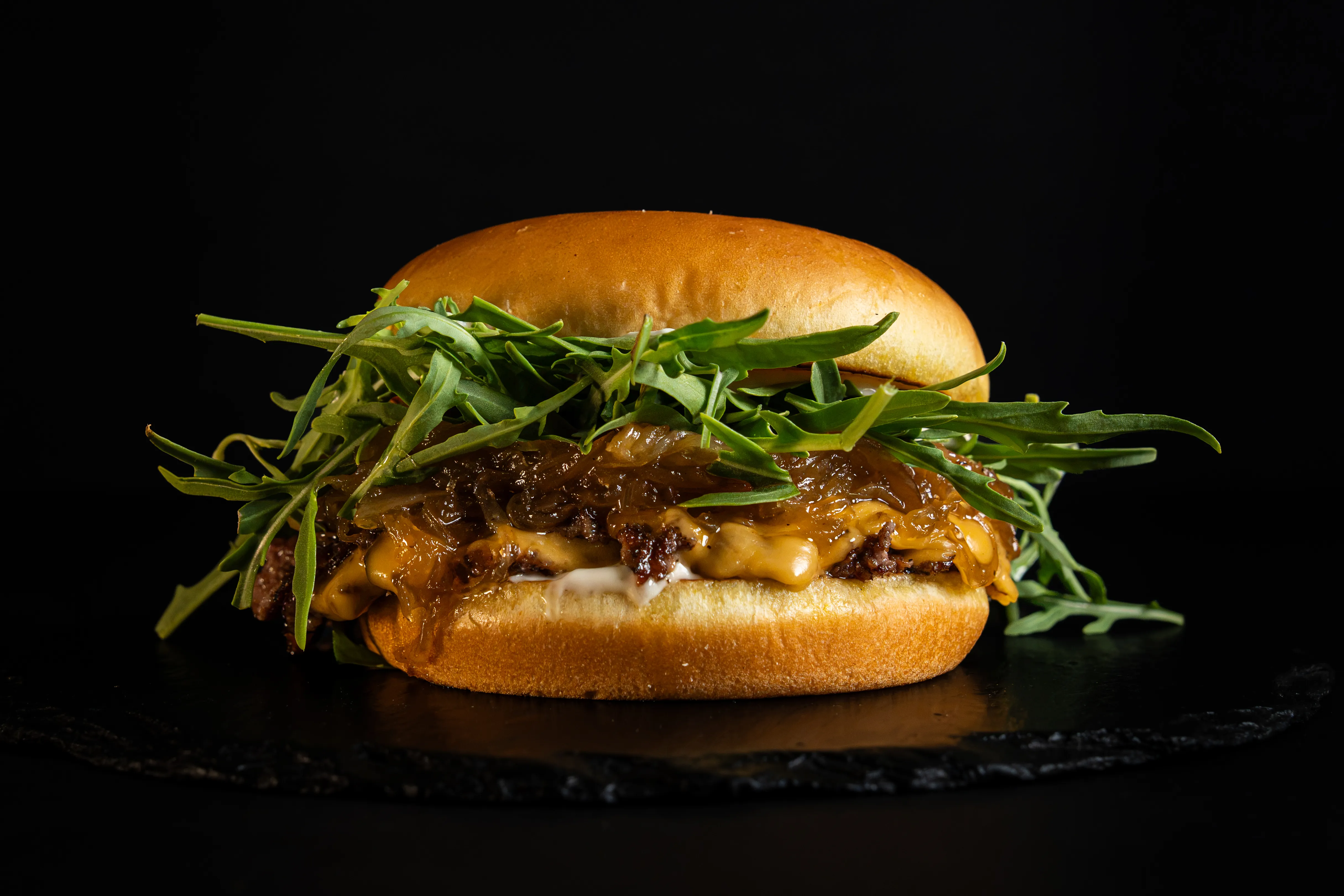 A burger topped with fresh rocket on a dark background