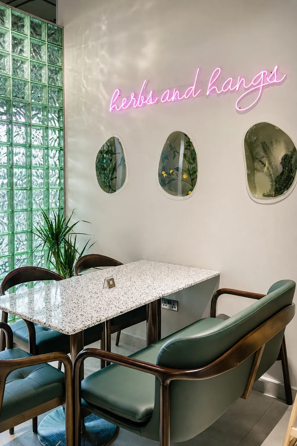 The Olive & Thyme dining room, with green upholstered chairs, a marble-topped table and a pink wall sign